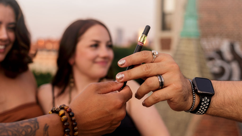 Closeup of a hand passing a Golden Tiger vape to another hand.