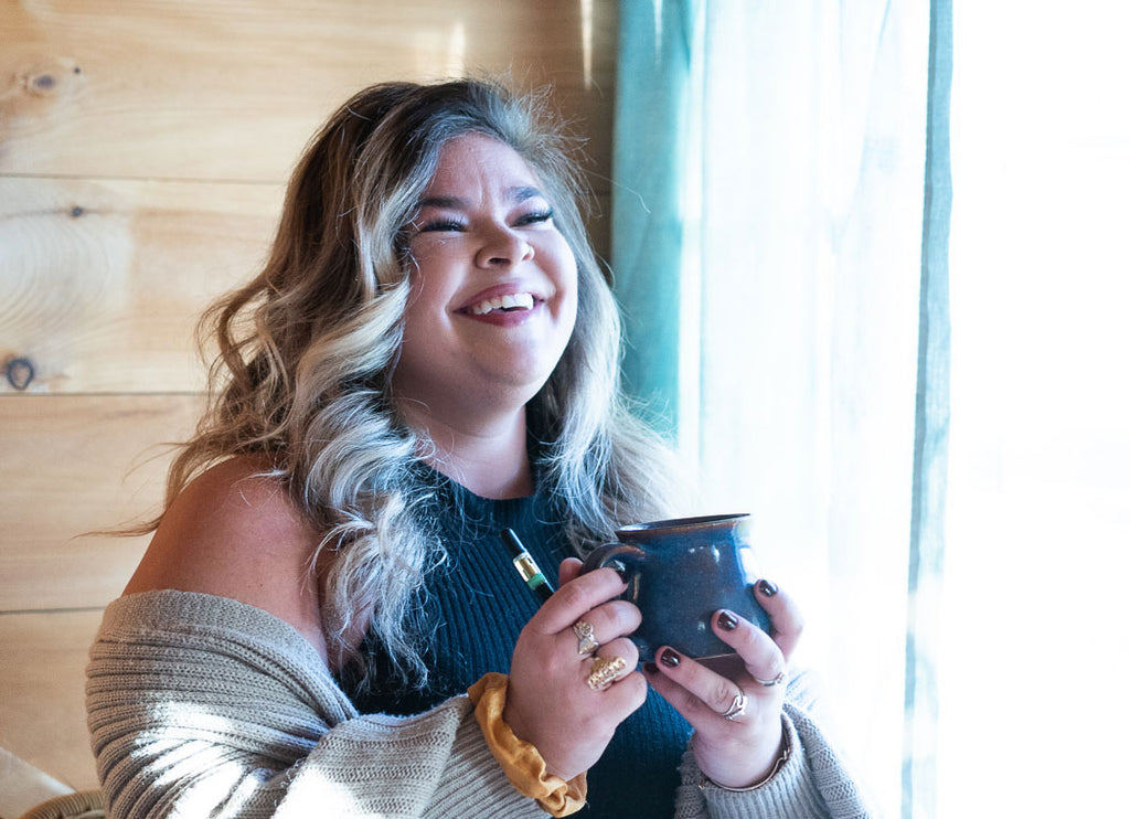 A woman smiling and holding a cup of tea and a Chocolate Mint vape.
