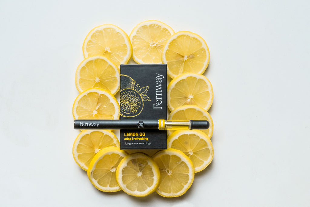 A full-gram Lemon OG vape resting on a Lemon OG box, which in turn is resting on a bed of sliced lemons.