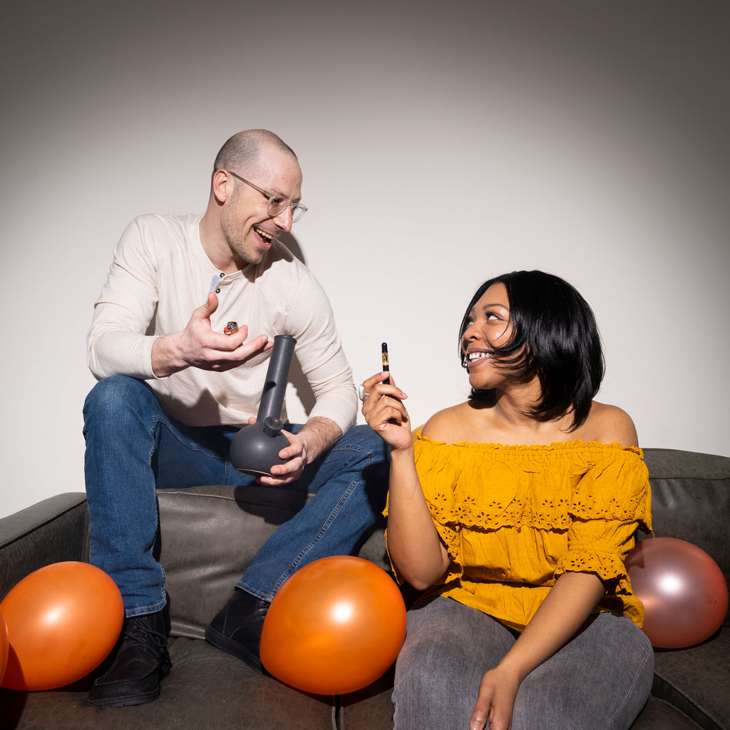 A man and a woman sitting on a couch enjoying a Mandarin Orange vape.
