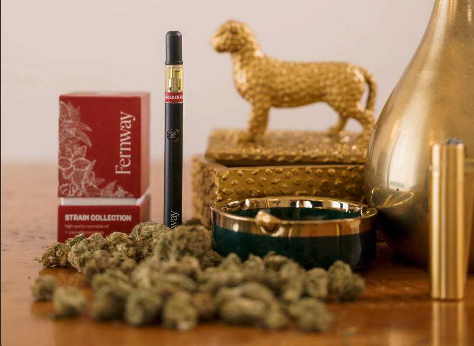 A closeup of a Golden Tiger vape and box surrounded by a gold lighter, a pile of premium flower, and a small statue of a Golden Tiger.